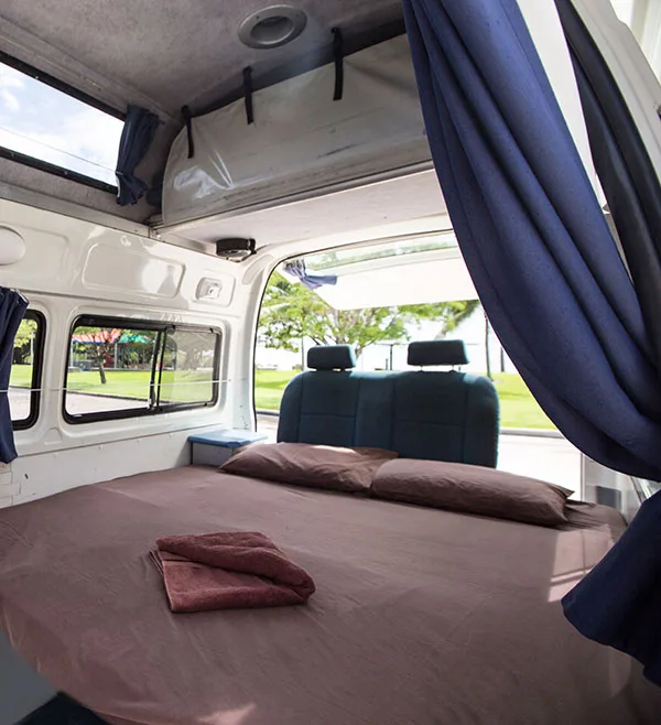 Inside a Camperman campervan showing the double bed made up with linen and curtained windows