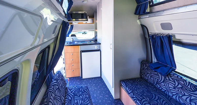 Inside a Camperman hi-top campervan showing the kitchen, fridge and seating area with blue upholstery