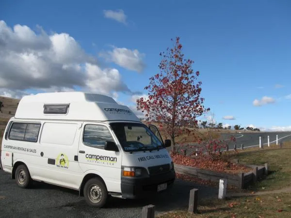 Camperman Australia branded campervan parked on an autumn road with a red tree in the background