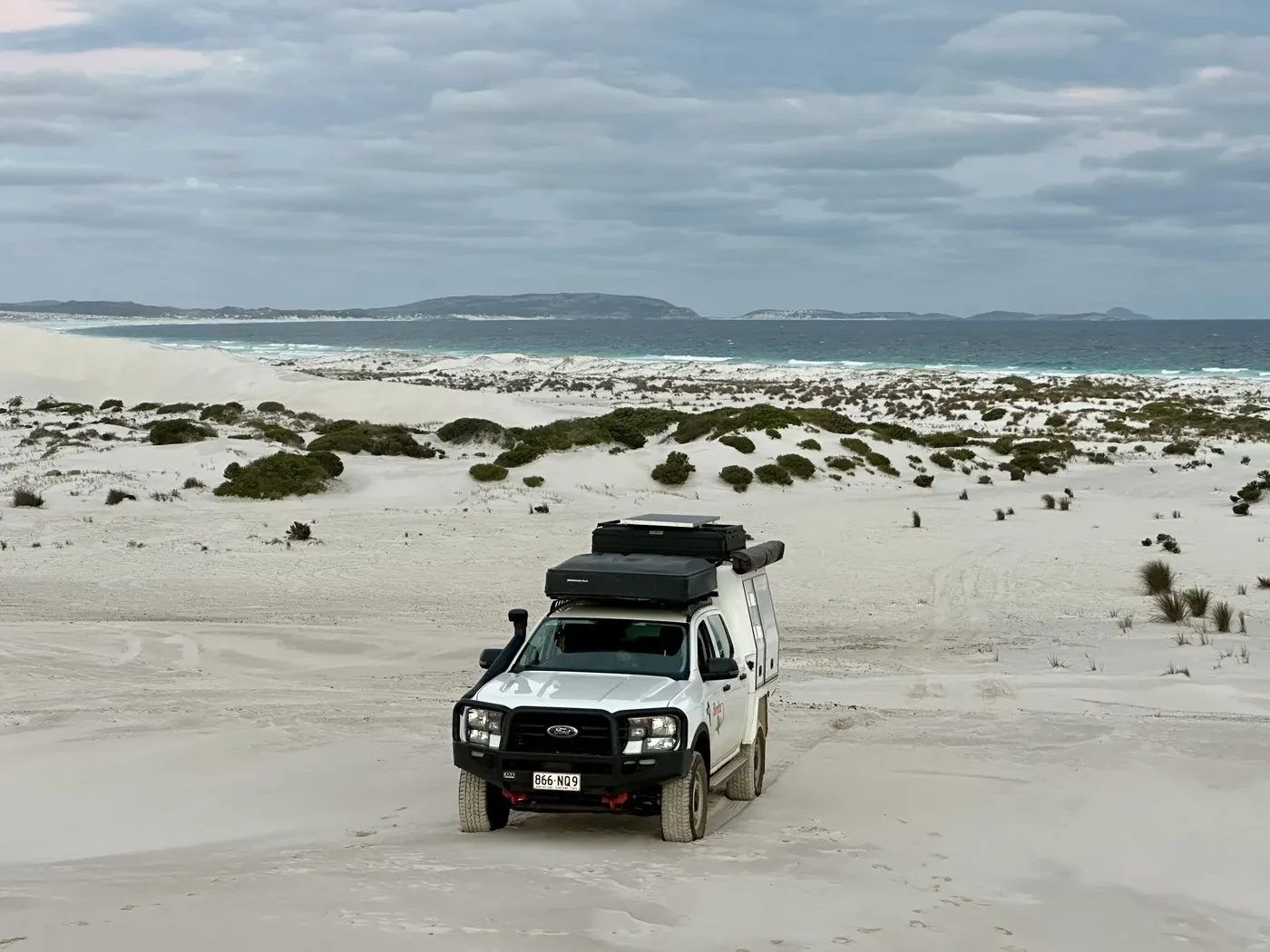 Britz 4WD Warrior driving through white sand dunes with turquoise ocean and islands visible in the background near Esperance