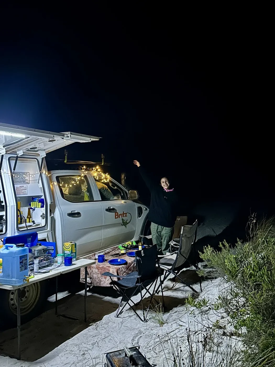 Woman sitting in the driver seat of a Britz 4WD Warrior looking out at turquoise ocean through the windshield at Lucky Bay