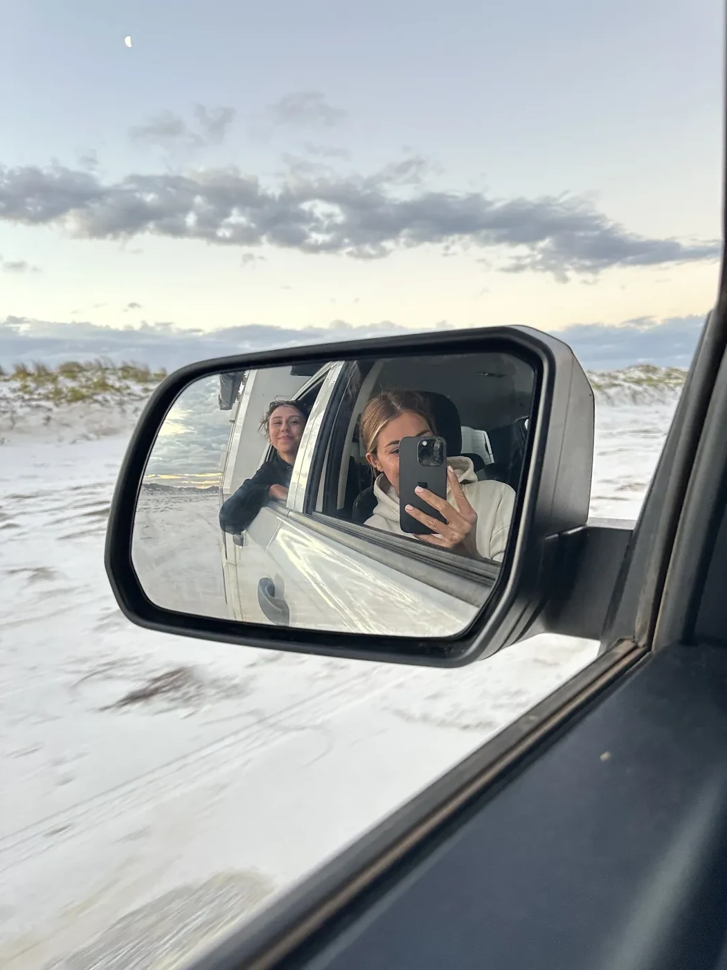 Two friends smiling in the side mirror of a Britz 4WD while driving along a white sand beach near Esperance