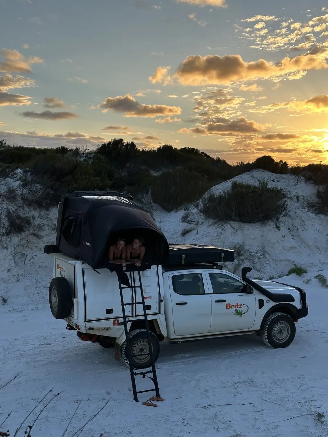 Night-time camp cooking setup beside a Britz 4WD Warrior on the beach with LED lights illuminating the kitchen area