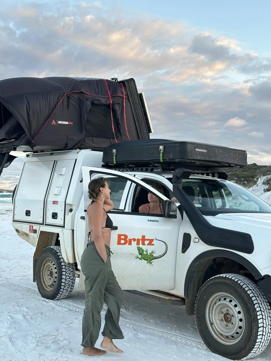 Britz 4WD Warrior with rooftop tent deployed among white sand dunes at sunset near Esperance, two travellers visible in the tent