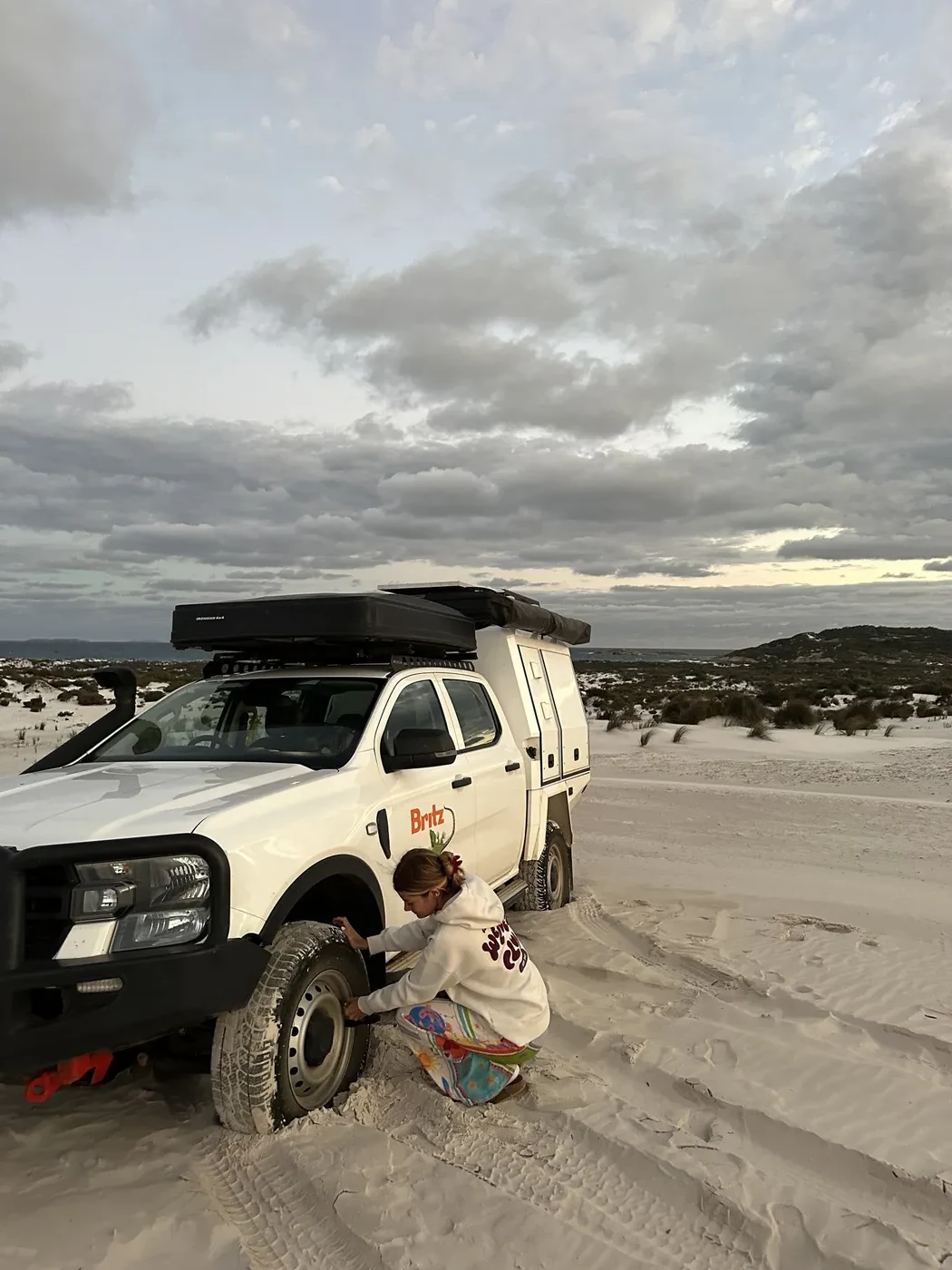 Traveller letting down tyre pressure on Britz 4WD Warrior before driving on beach sand near Esperance