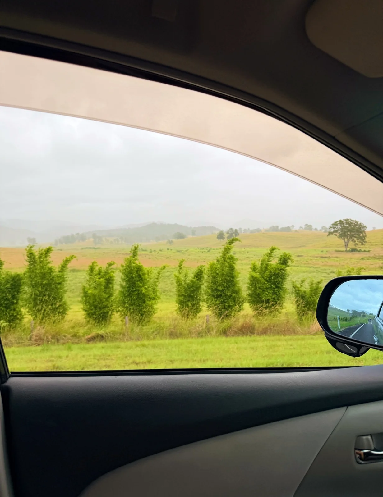 View from the passenger seat of a Spaceship Beta driving through green rolling hills on the Sunshine Coast hinterland, pink gingham skirt and legs visible